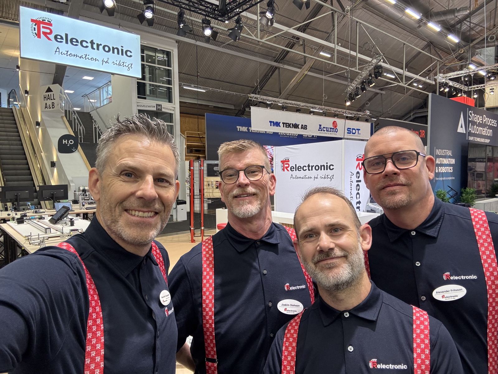 Henrik Carpevi, Joakim Olofsson, Fredrik Nylander och Alexander Fritsson från TR Electronic i mörkblå pikéer och röda hängslen framför montern på Svenska Mässan